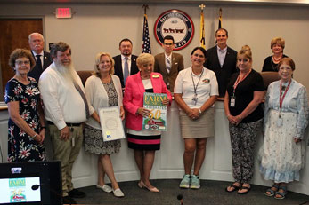Image of the County Commissioners with representative from the Farm Museum standing in front with a proclamation and 6th anniversary poster